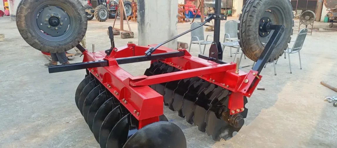 Red disc harrow with black disc gangs and raised transport wheels in a machinery area